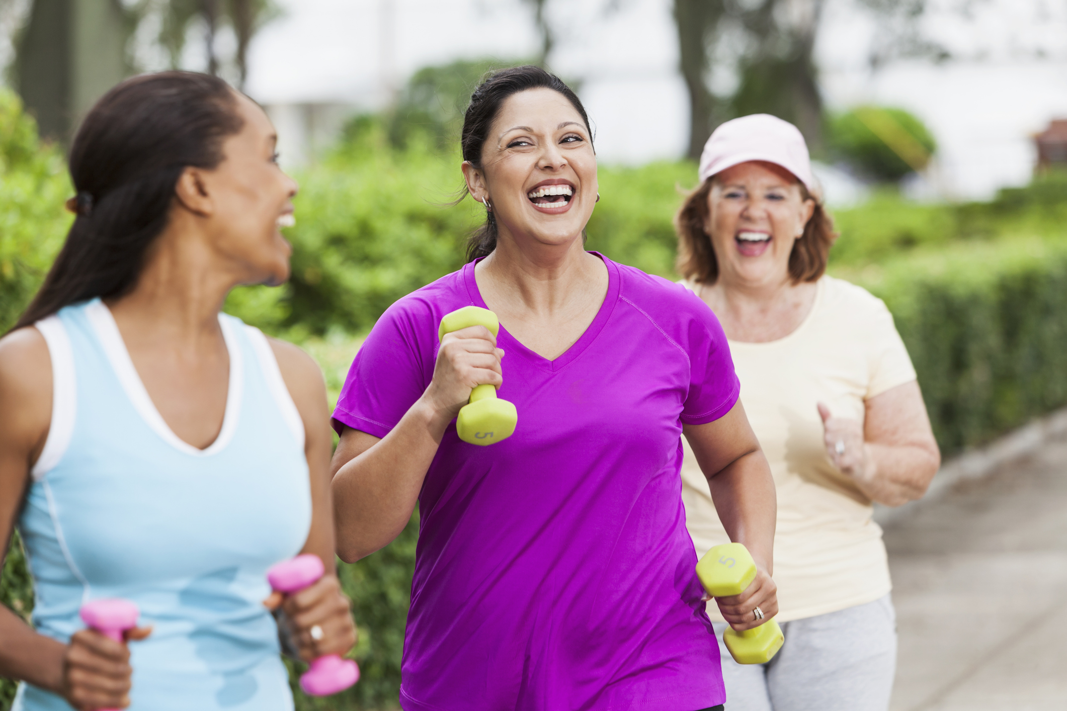 Multi-ethnic women (30s, 40s, 60s) exercising in park, power walking.  Hispanic woman in middle (30s).